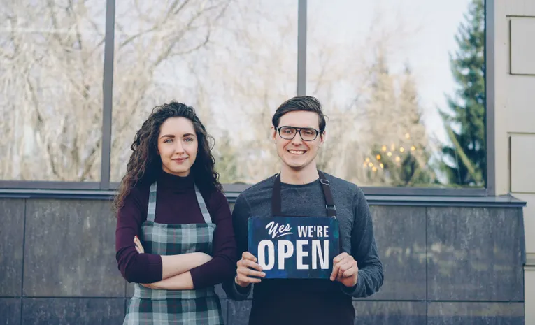 Small business owners holding an open sign outside their shop
