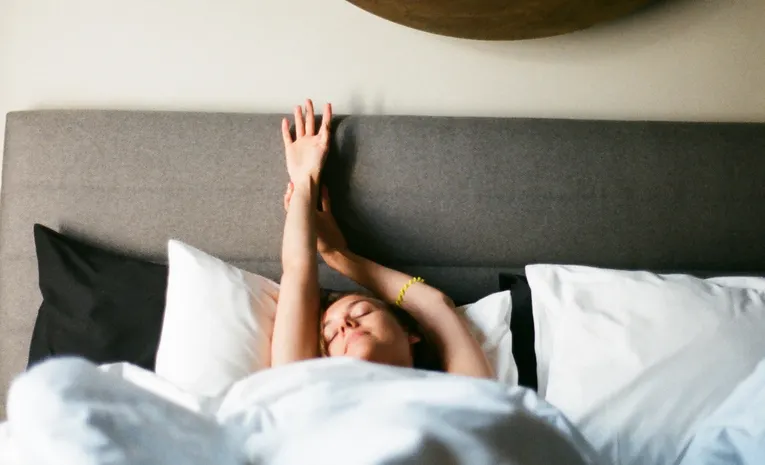 Person stretching in bed with morning sunlight
