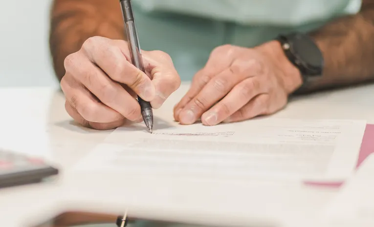 Person signing a formal document at a desk